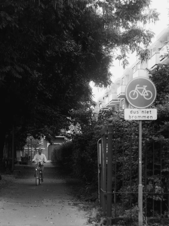 black and white po of man on bicycle passing by a building