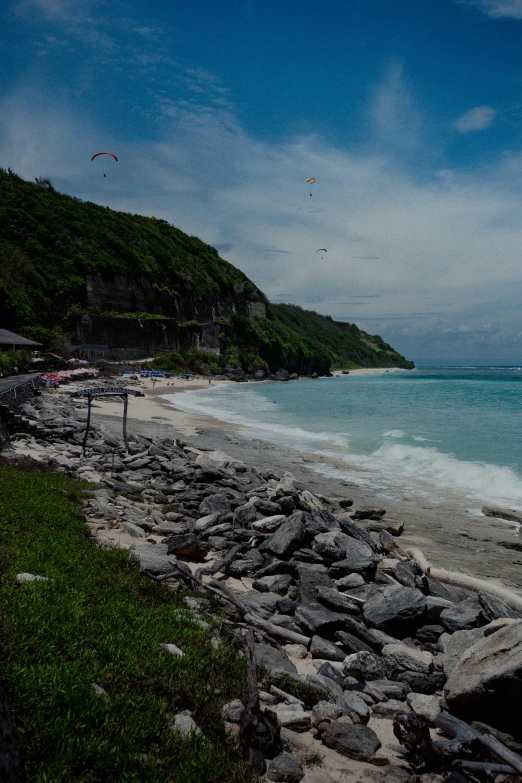 the sky is full of clouds, with kites flying above the beach