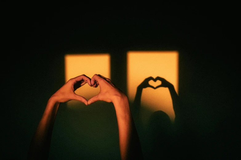 someones hands forming a heart shaped shape in front of a shadow of two people