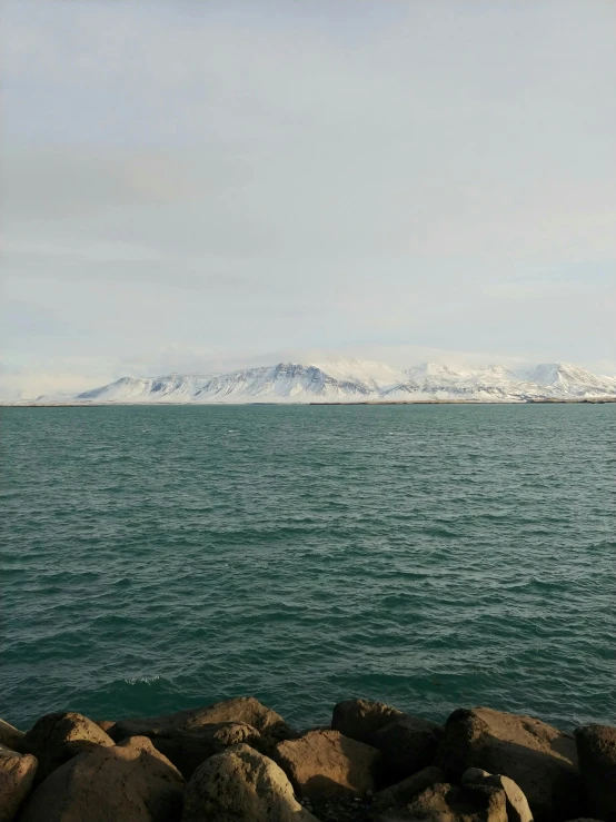 mountains behind the water with rocks and snow