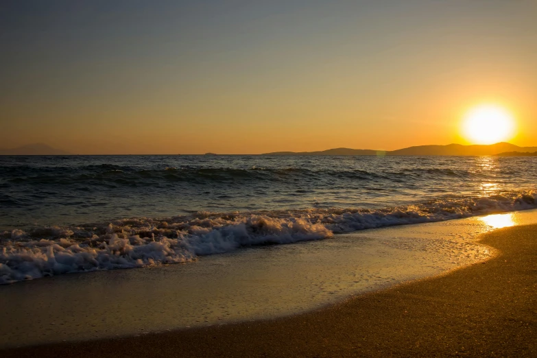 a sunset is reflected on the water as waves roll on a sandy beach