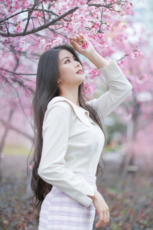 a woman wearing a white shirt standing in front of pink flowers