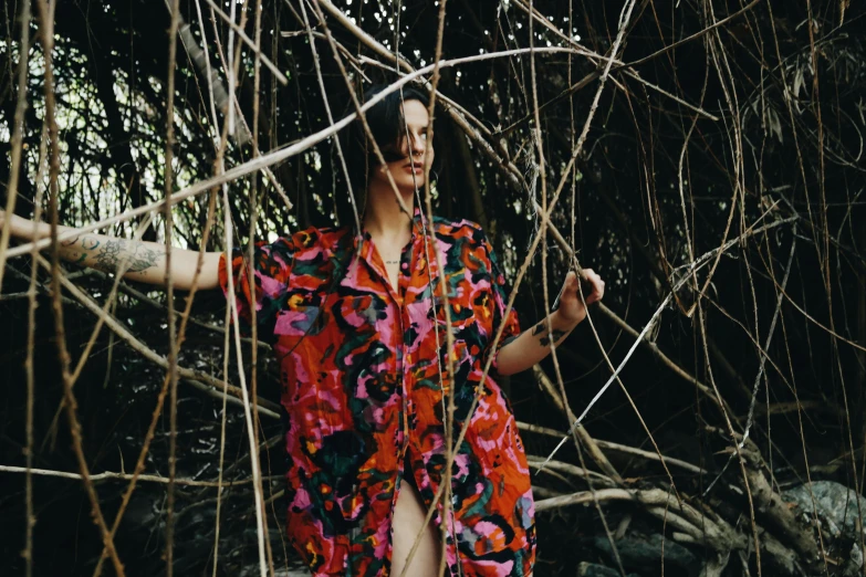 a lady standing through some thin nches in the woods