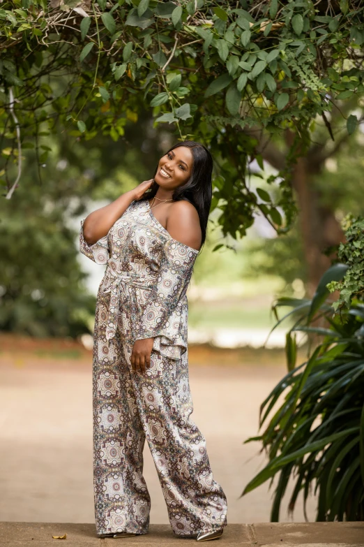 a woman poses in a very large jumpsuit in front of some trees