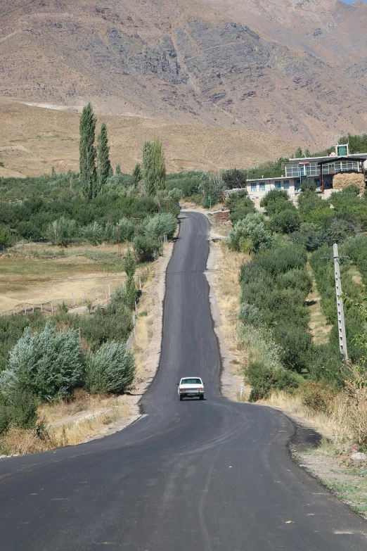 a car on a lonely road between a mountain and a residential area