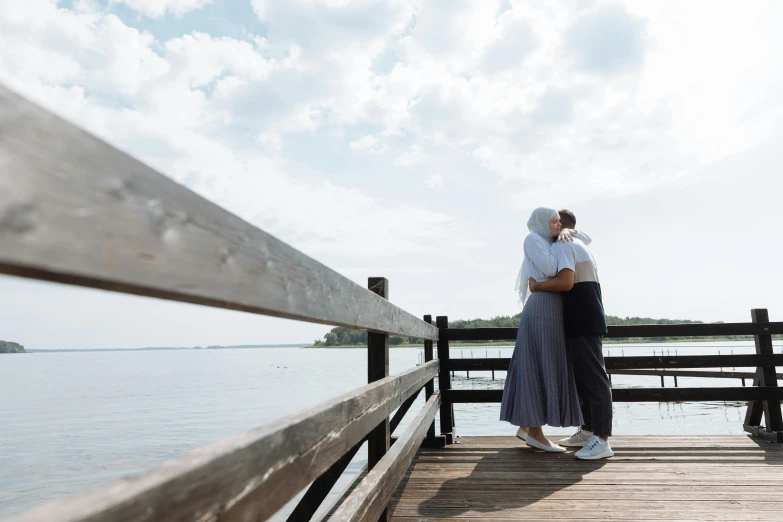 couple hugging while standing on a pier next to the water