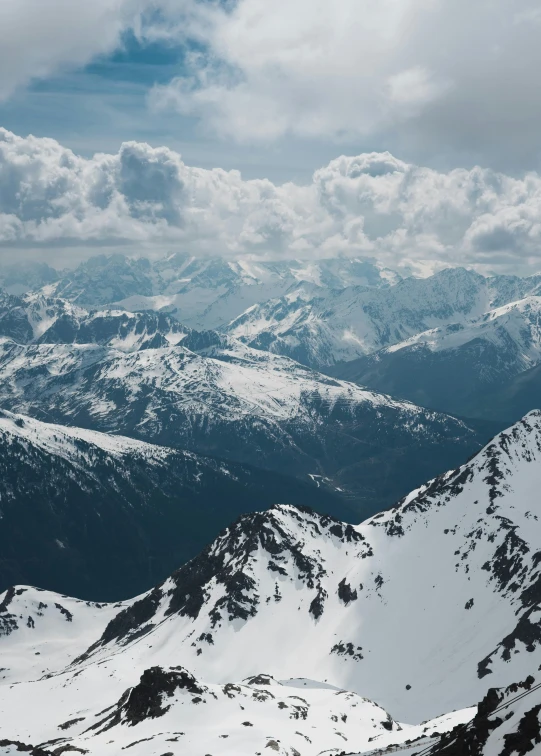 a mountain range with snow capped mountains under a cloudy sky