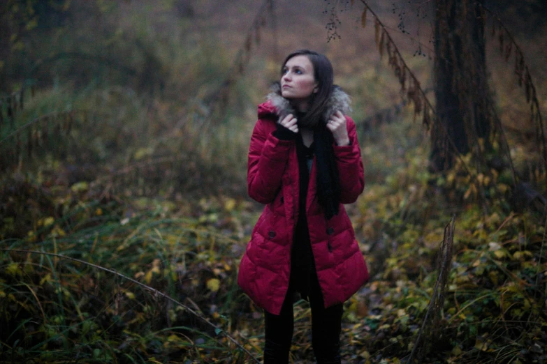 a young woman wearing a red coat standing in a forest