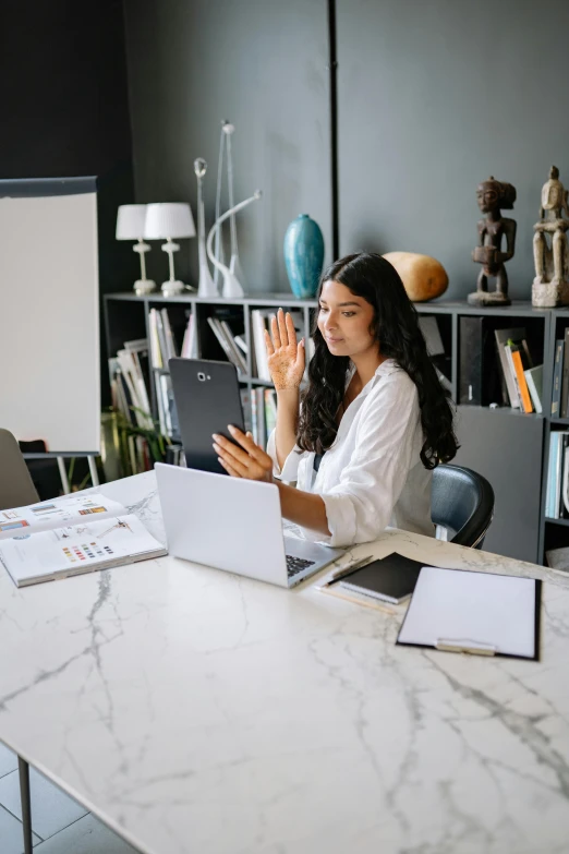 a woman is sitting at a table with two laptops