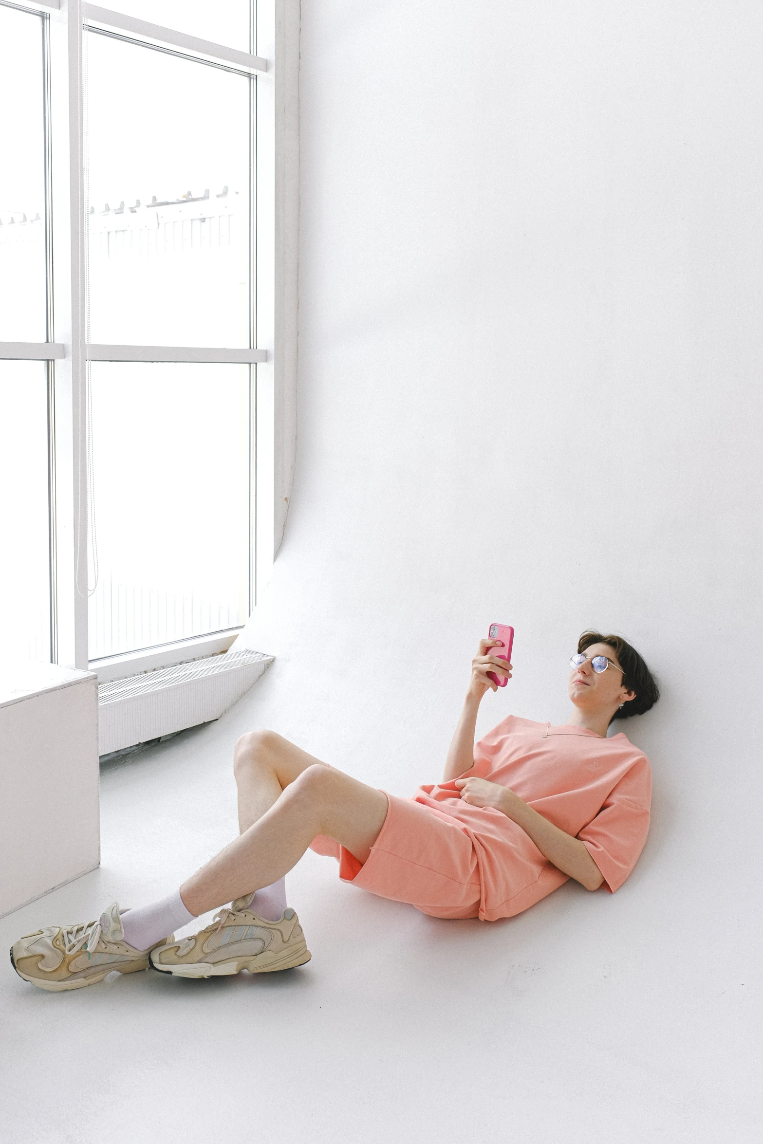 a young woman in glasses and an orange shirt laying down holding up her phone