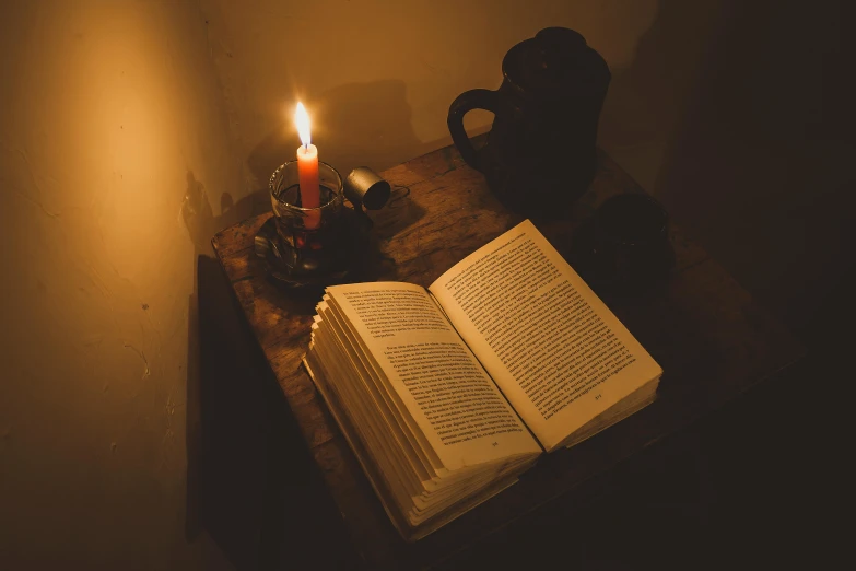 an open book and a lit candle sit on a table