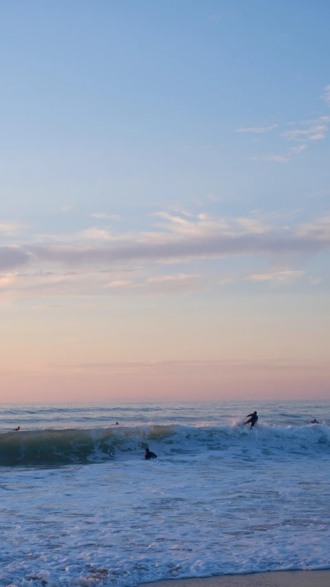 a person is walking on the beach as two surfers are waiting