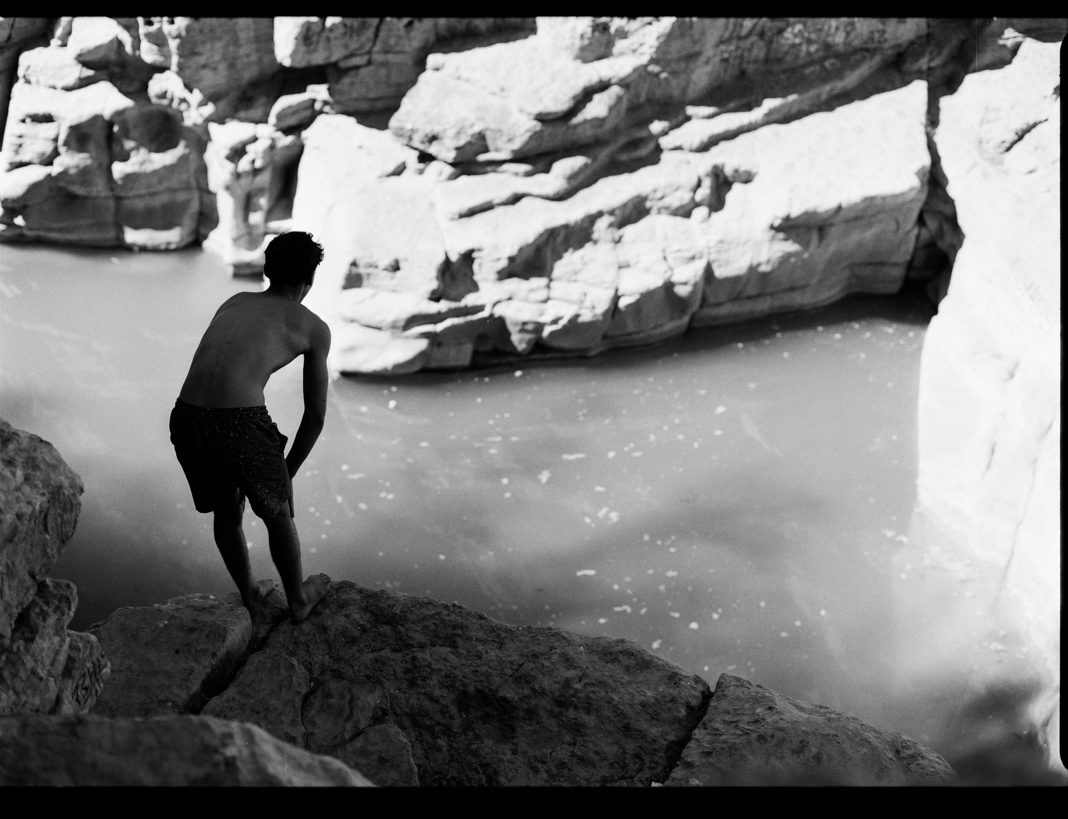 man in bathing suit standing on a cliff near water