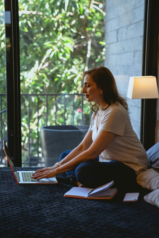 a woman is sitting on her bed with a laptop in her lap