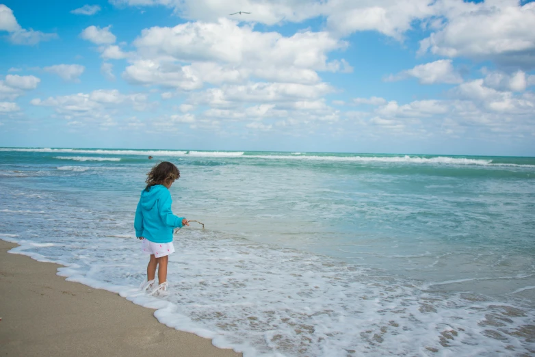 a woman is standing at the ocean edge and holding a kite