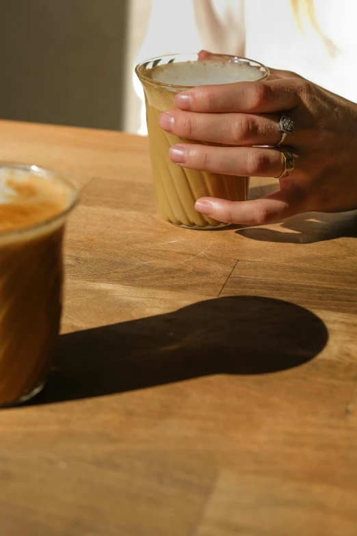 a person holding onto a glass with their hand on the table