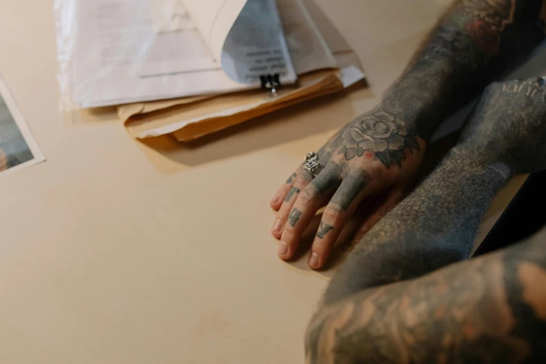 a hand with tattoos holding a cigarette with soing in the background