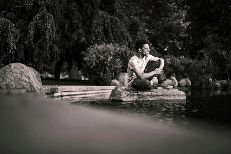 man sitting on rocks in pond surrounded by trees