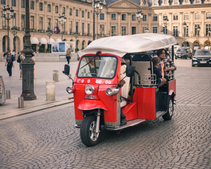 a small red three wheeled tukgo in a busy area