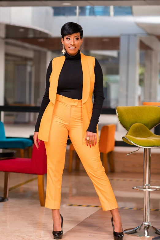 a woman in yellow pants and black sweater standing near chairs