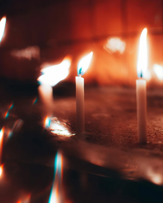 white candles sitting on a table in front of a lit fireplace