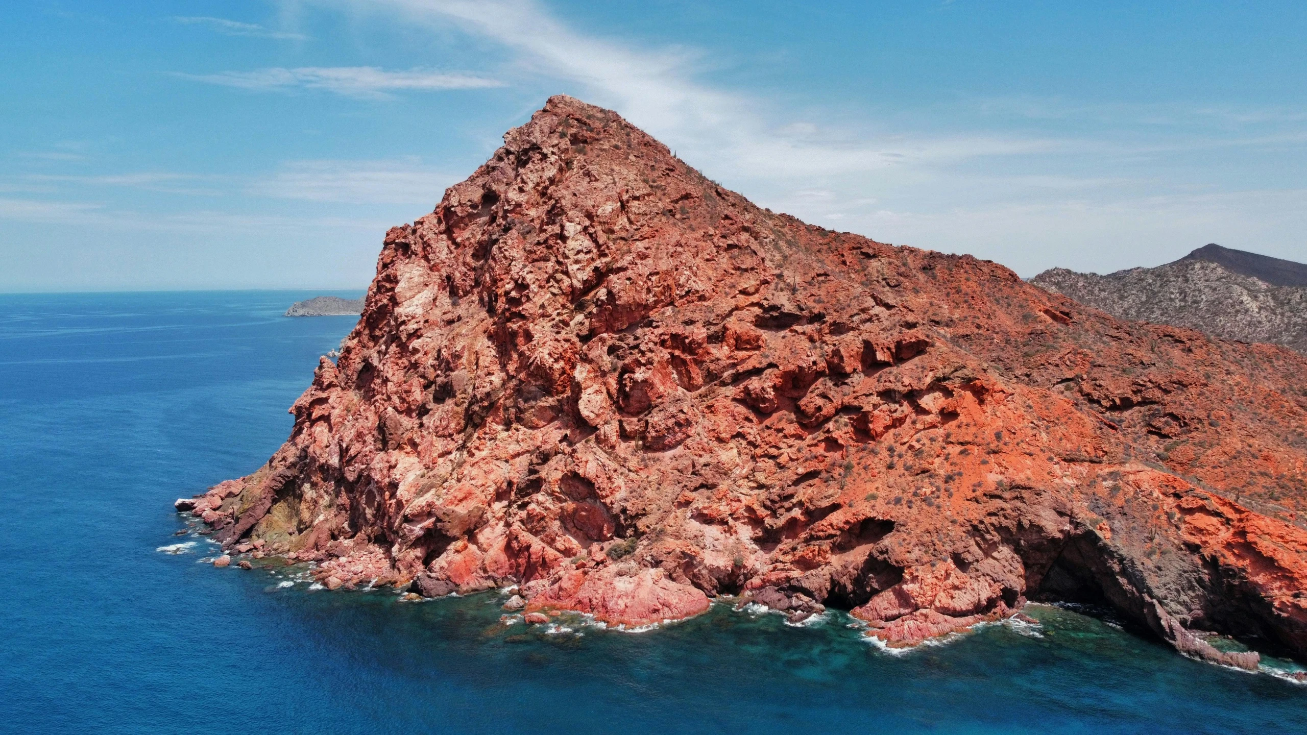 a large red mountain with sea in the background