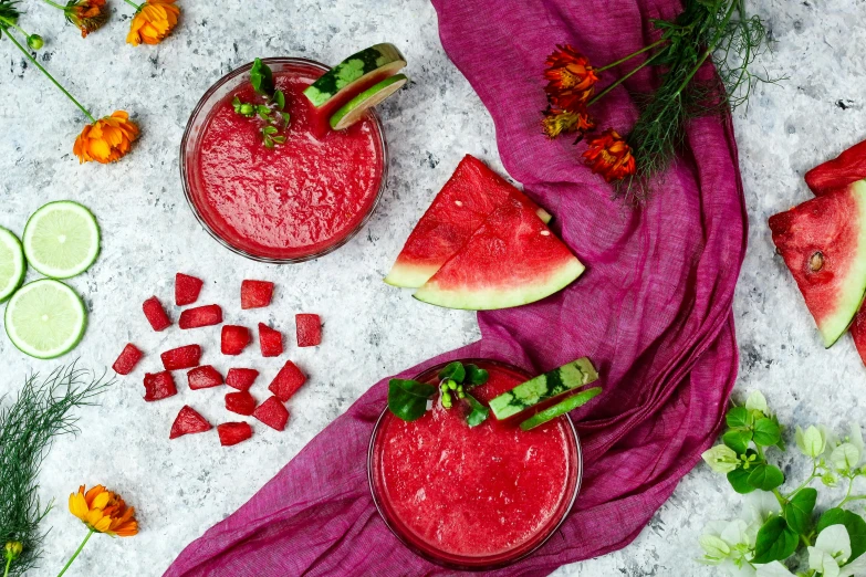 a table topped with two pink cocktails next to a sliced watermelon