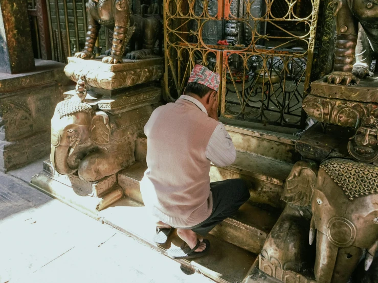 a man kneeling in front of a gate next to a statue