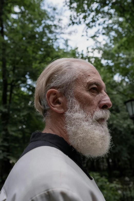 an older man with a white beard in front of trees