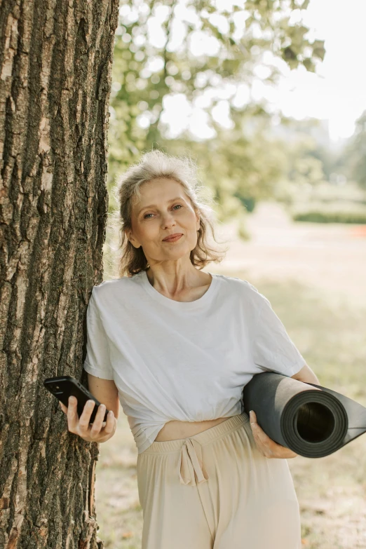 a woman leaning against the side of a tree holding a black umbrella