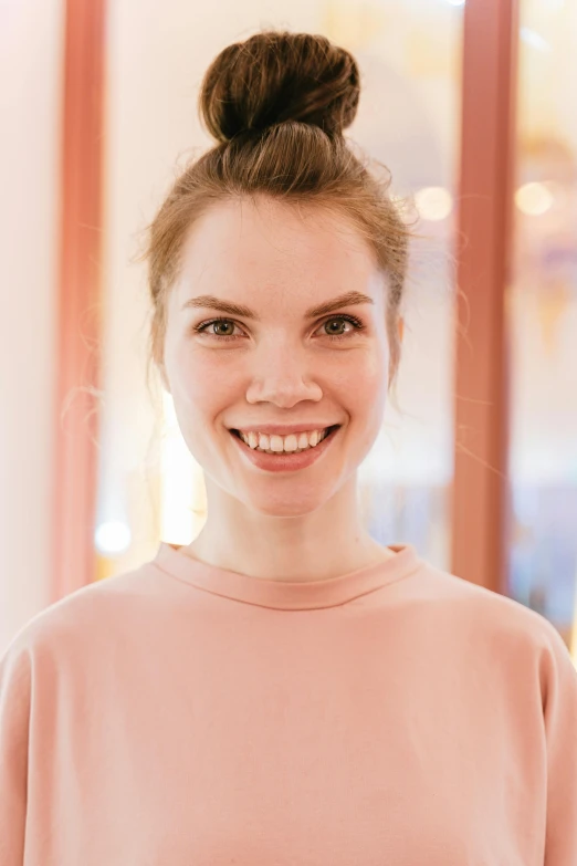 a smiling woman wearing a pink sweatshirt in front of a window