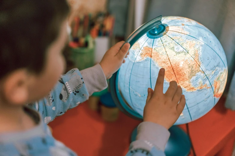 a little boy pointing at the globe he is holding