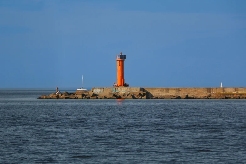 the lighthouse is orange and red next to the ocean