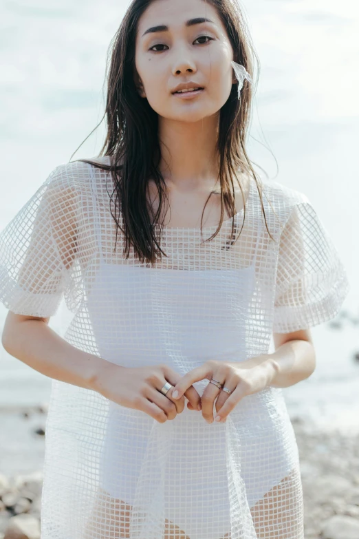 a woman standing on a beach with her hands folded around the waist