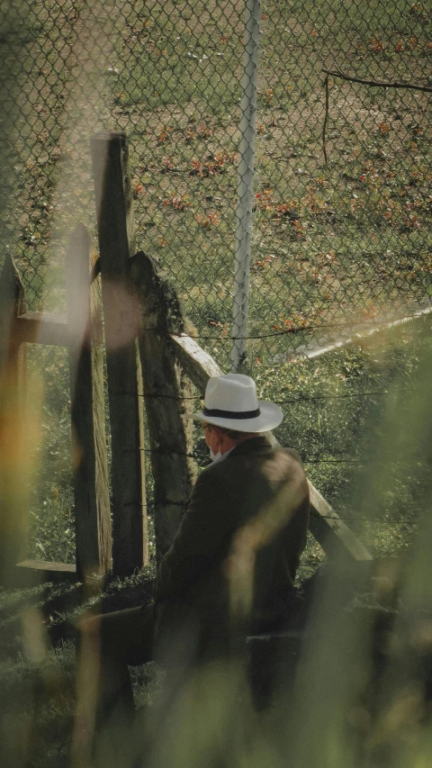 a man is sitting outside beside a wooden fence