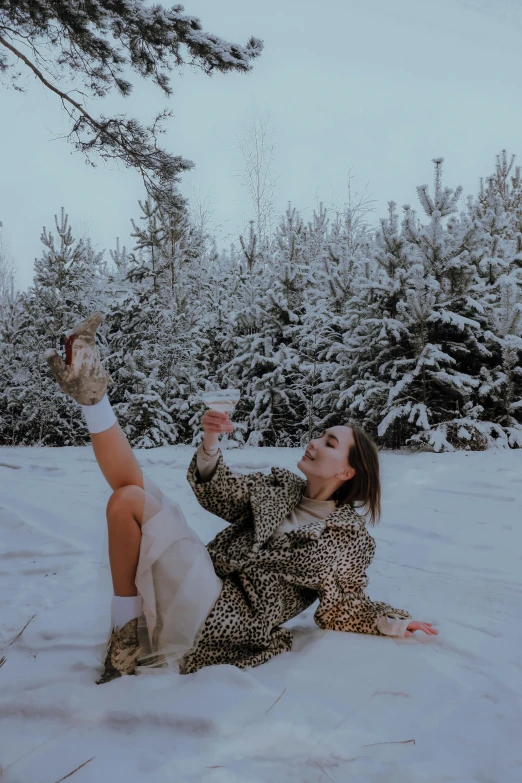 a woman sits on snow in a fuzzy dress and holds onto a beverage glass