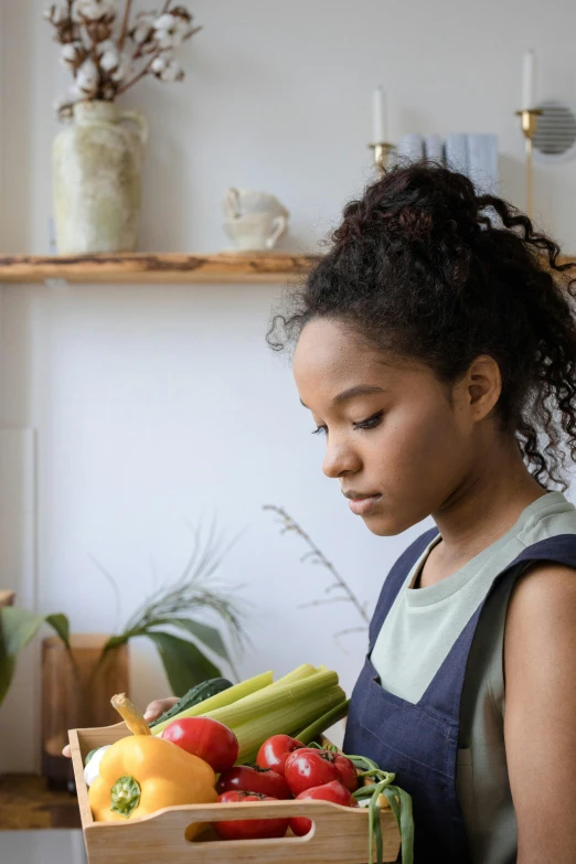 a girl holding a box of vegetables on a kitchen counter