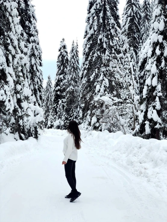 a woman in white shirt walking in snow next to evergreen trees