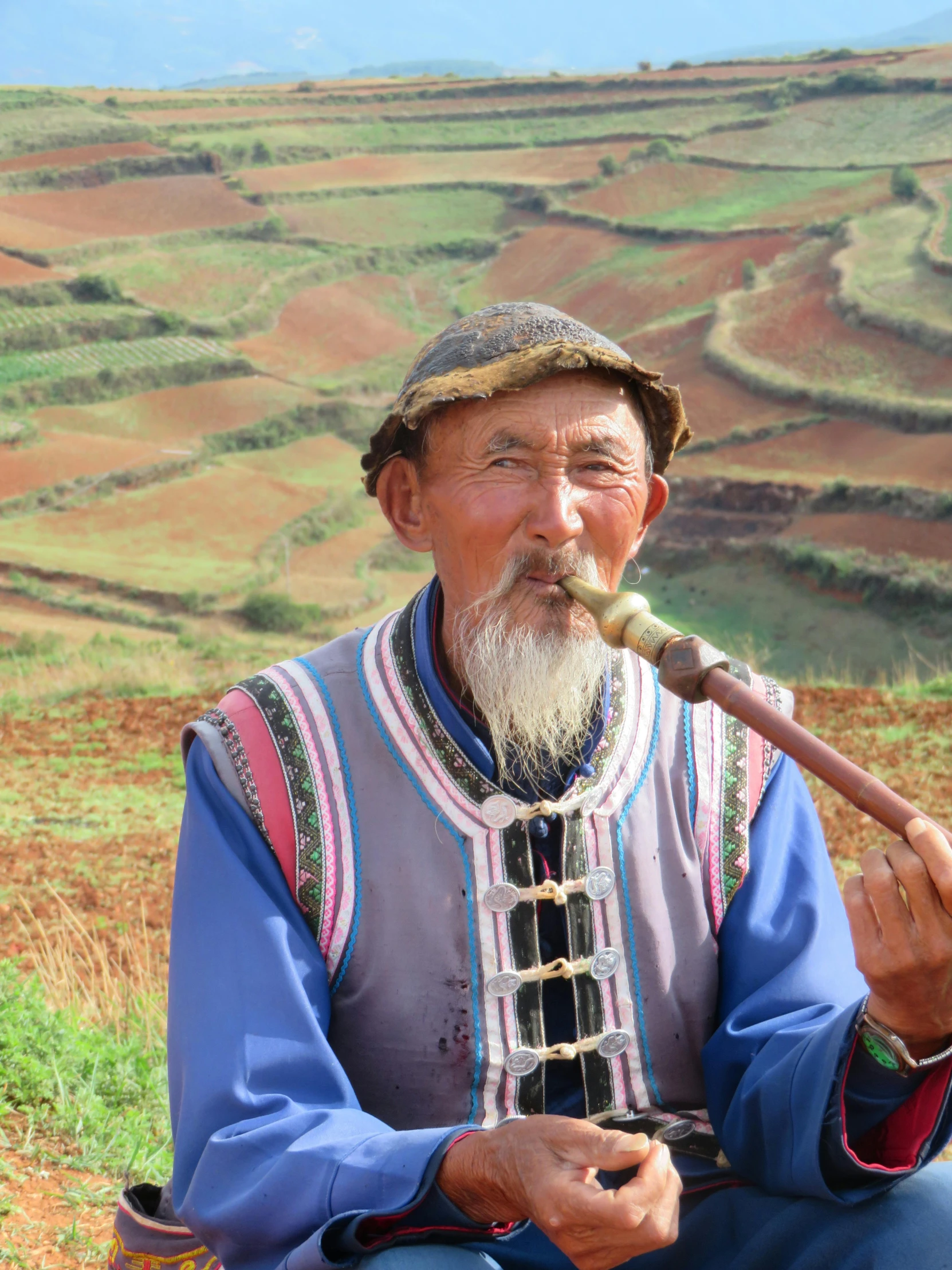 an elderly man holding a pipe sits in a field