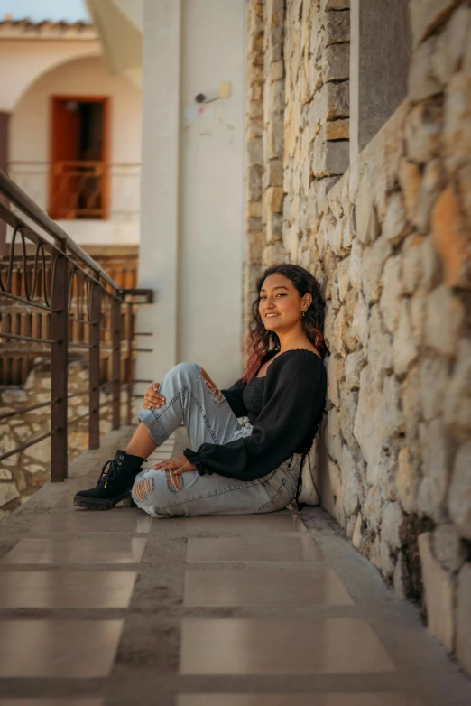 a woman smiling while sitting on the ledge in front of a building