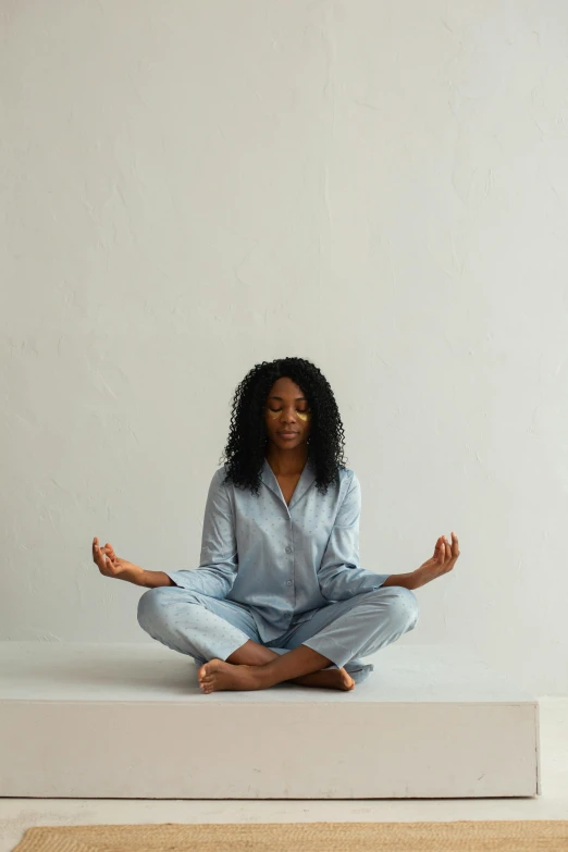 a woman in a blue shirt and pants sitting on the ground while doing yoga
