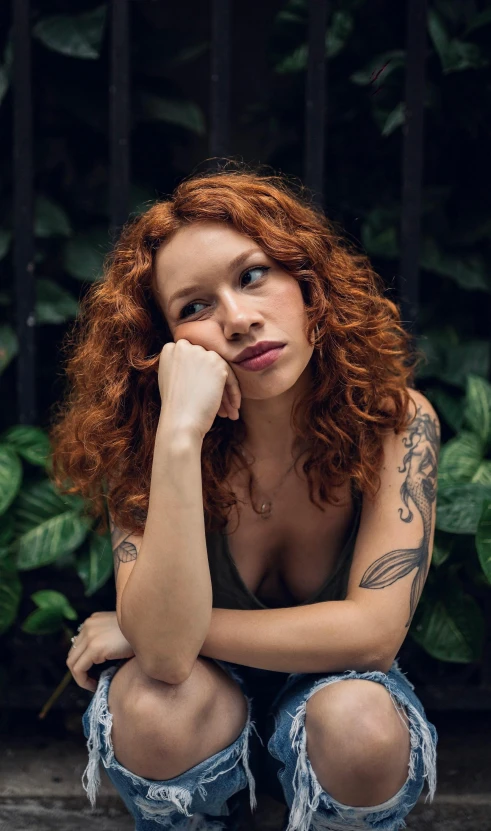 a woman with red hair and tattoos sits on the ground with her arm propped up