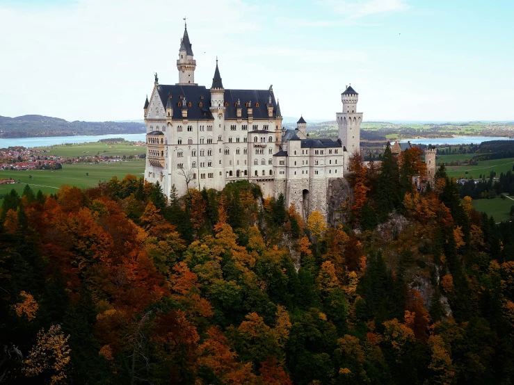 an old castle with several towers stands atop an autumnal hill