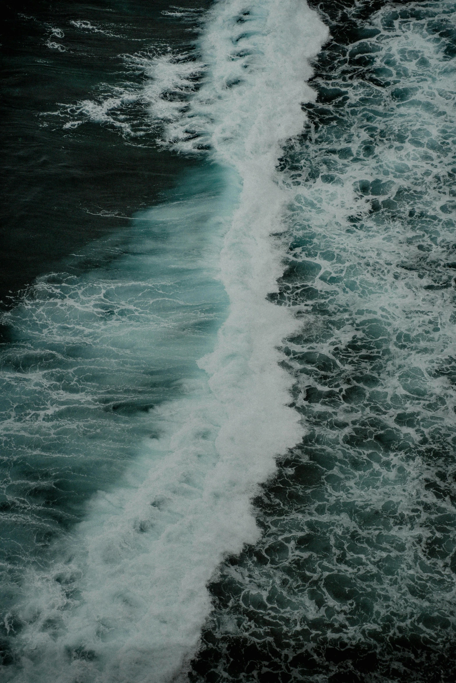 a small wave moves towards shore on a black beach