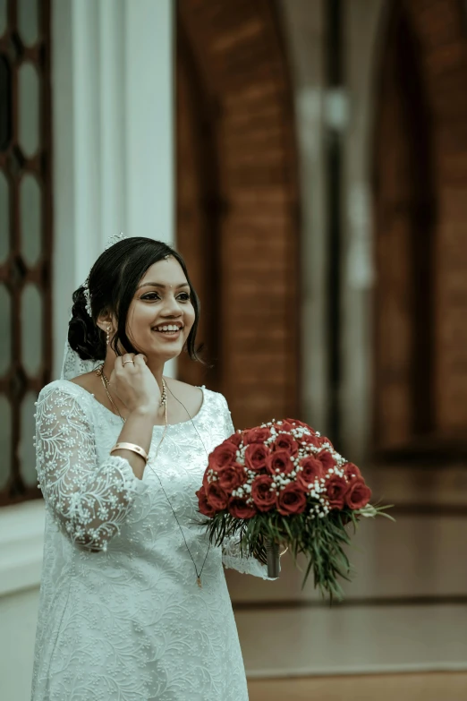 a woman in a white dress and a bouquet smiles as she puts on her wedding ring