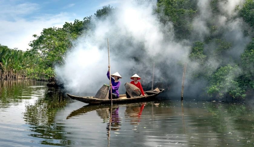 two people in a small canoe with smoke rising from the shore