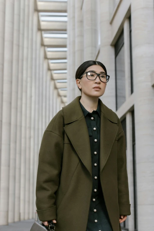 a woman is standing outside wearing black pants and an olive green coat