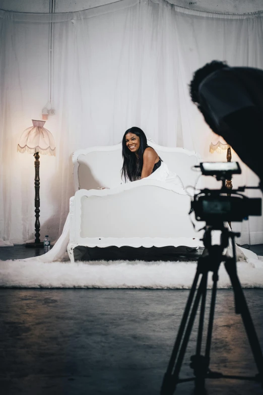 camera woman in white room sitting on couch with white sheet
