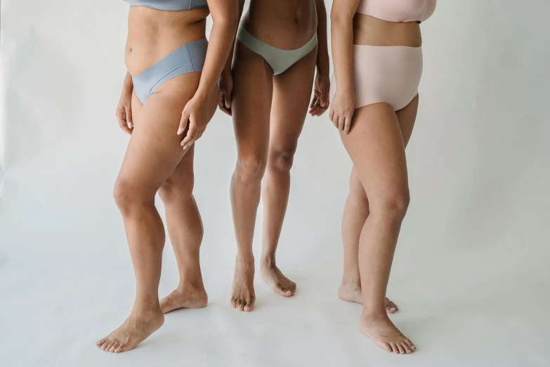 three people pose in bikinis against a white backdrop