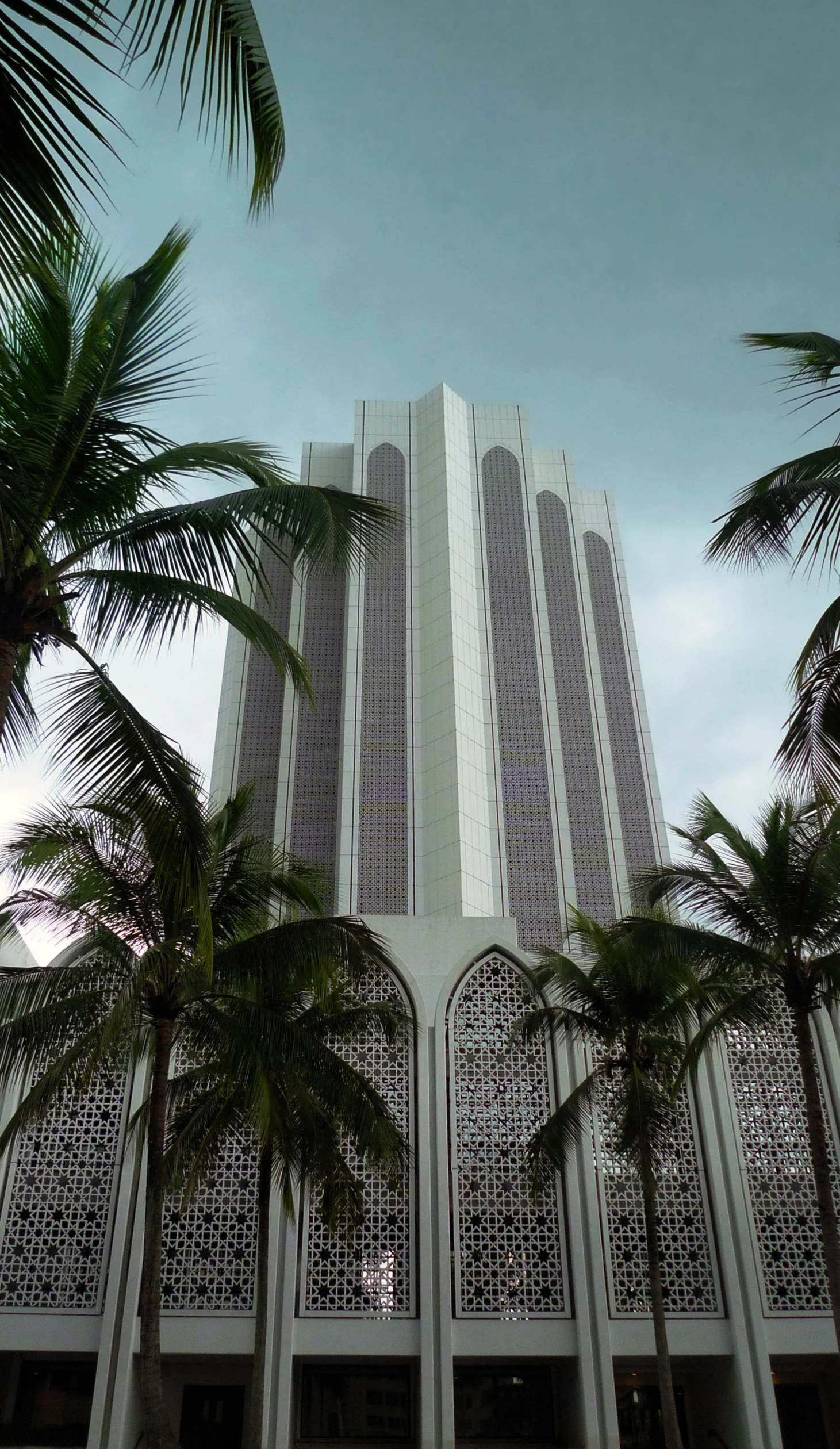 a tall building with a lot of windows next to a row of palm trees